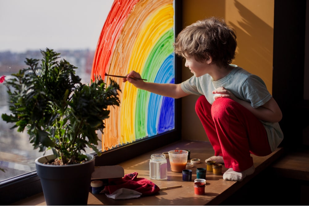 child at home draws a rainbow on the window